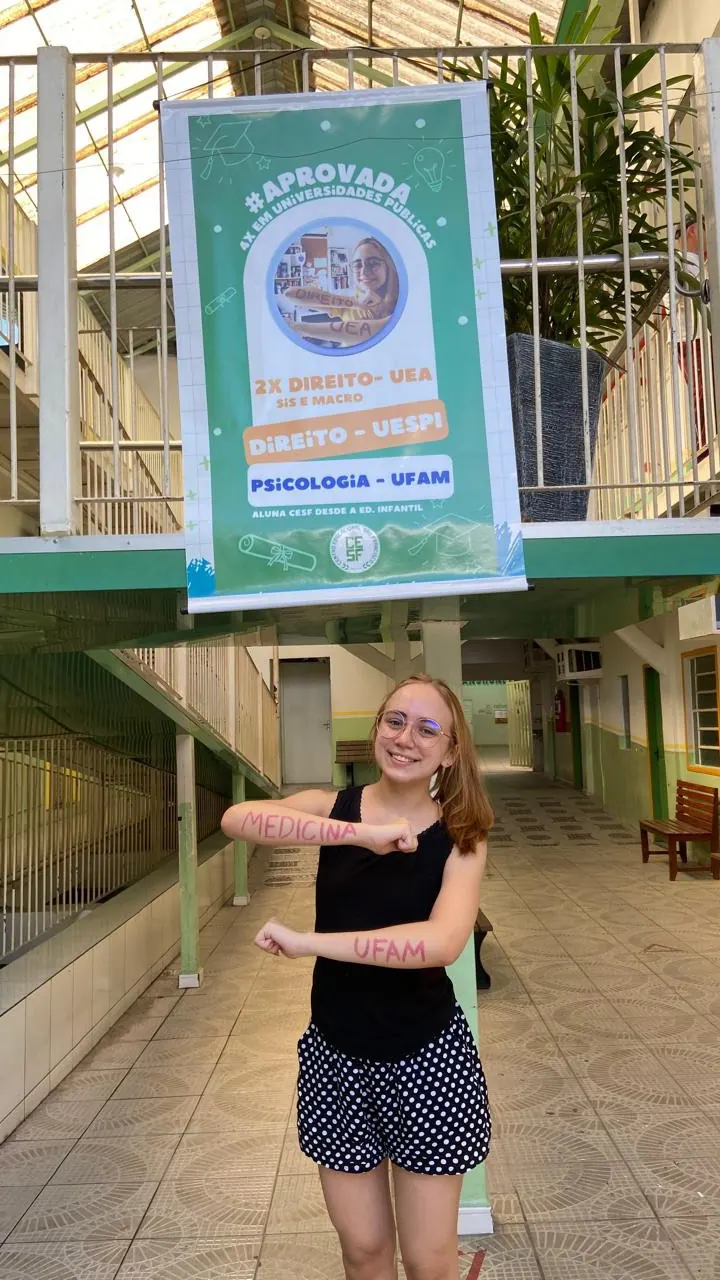 Aluna do CESF comemorando aprovação em Medicina na UFAM, em frente ao banner de aprovações